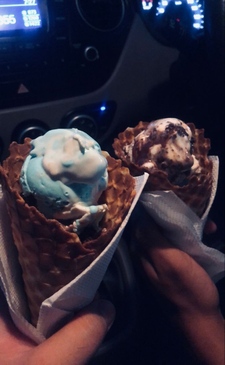 two ice cream cones with blue and white toppings are held up by someone's hand