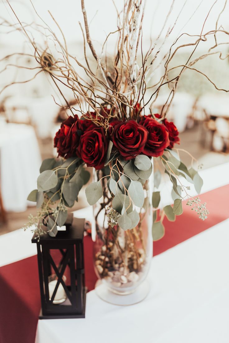 a vase filled with red roses sitting on top of a white table covered in greenery