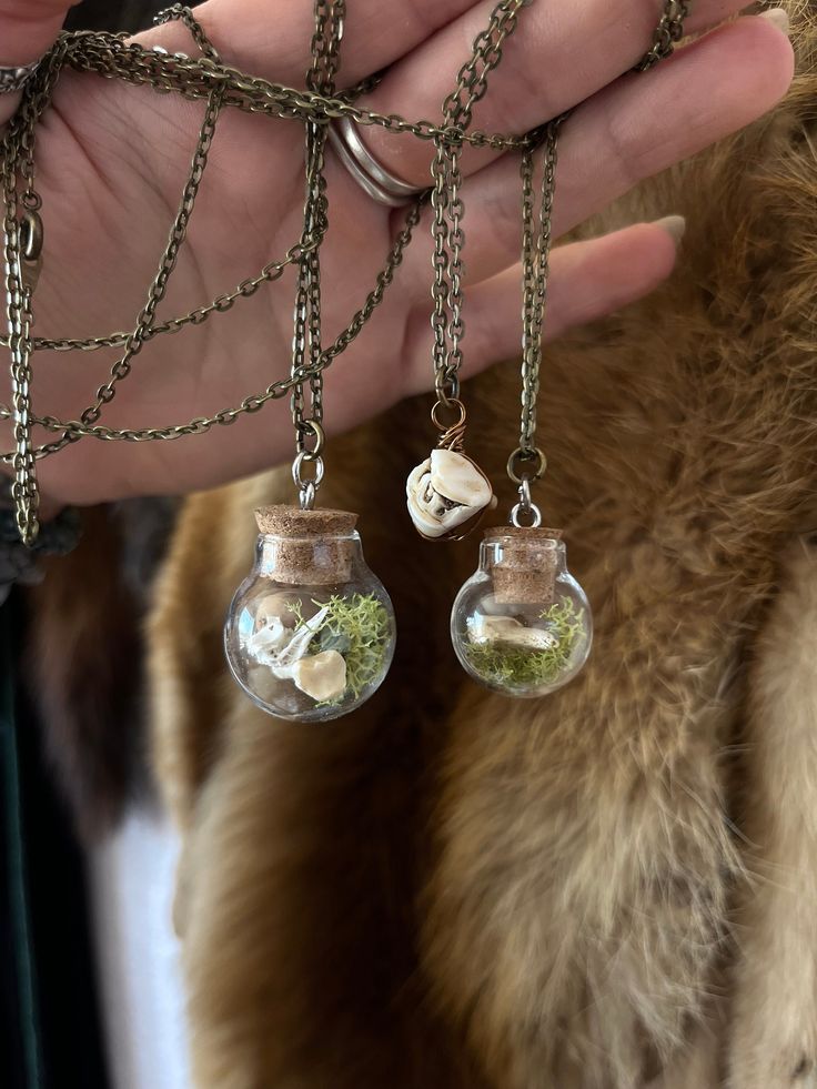 Three jewelry items made from natural wonders: Appalachian Deer Tooth: this amulet is a deer molar found in the northern Appalachians, suspended on an 18 inch chain. Large Bottle: a round glass bottle containing a fish vertebra, coyote toe bone, and reindeer moss, suspended on a 30 inch chain. Smaller bottle: a round glass bottle containing a coyote claw and reindeer moss, suspended on a 30 inch chain. Nature-inspired Healing Necklace With Round Pendant, Healing Charms Round Pendant Necklace, Reindeer Moss, A Deer, Small Bottles, Glass Bottle, Natural Wonders, Glass Bottles, Round Glass