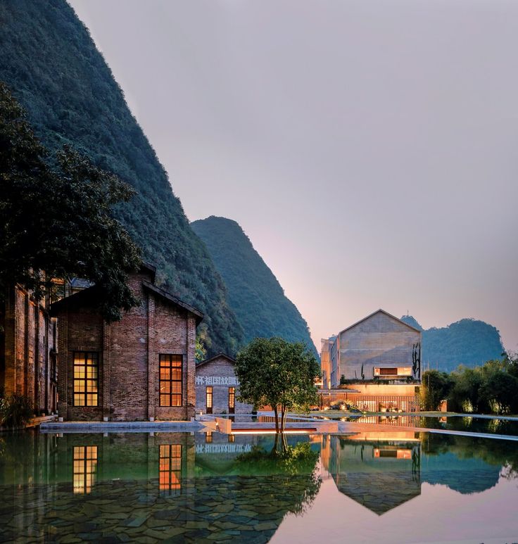 an outdoor swimming pool surrounded by mountains and trees at dusk with buildings in the background