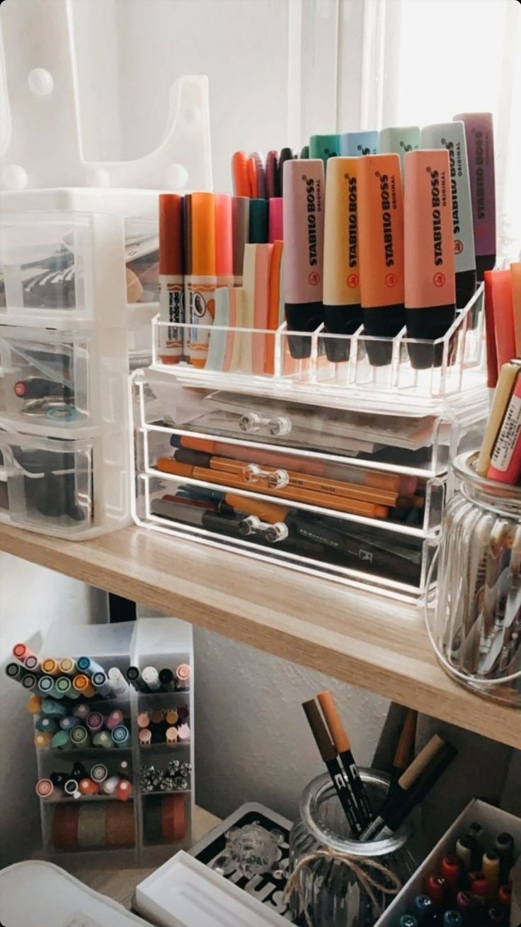 an organized desk with pens, markers and pencils in containers on the shelf next to a window