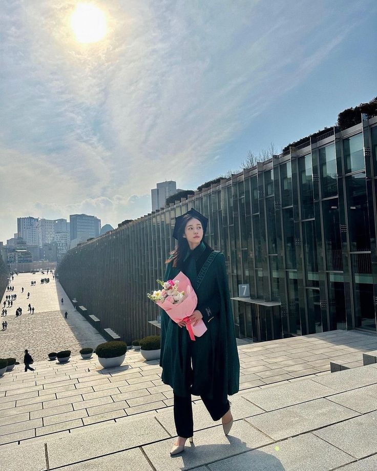 a woman standing in front of a large building holding a bouquet of flowers and looking at the camera