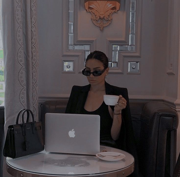 a woman sitting at a table with a laptop and cup in front of her face