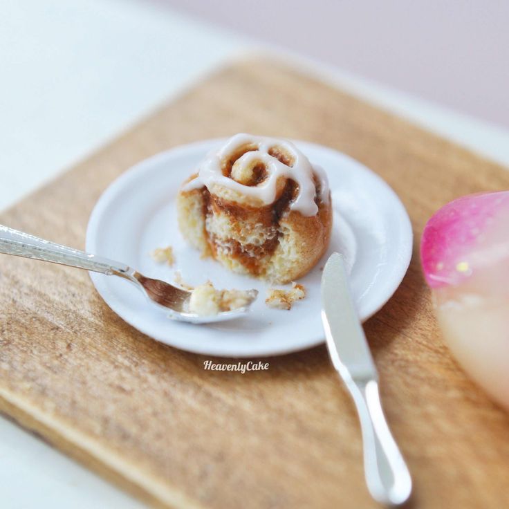 a small cinnamon roll sitting on top of a white plate next to a pink flower