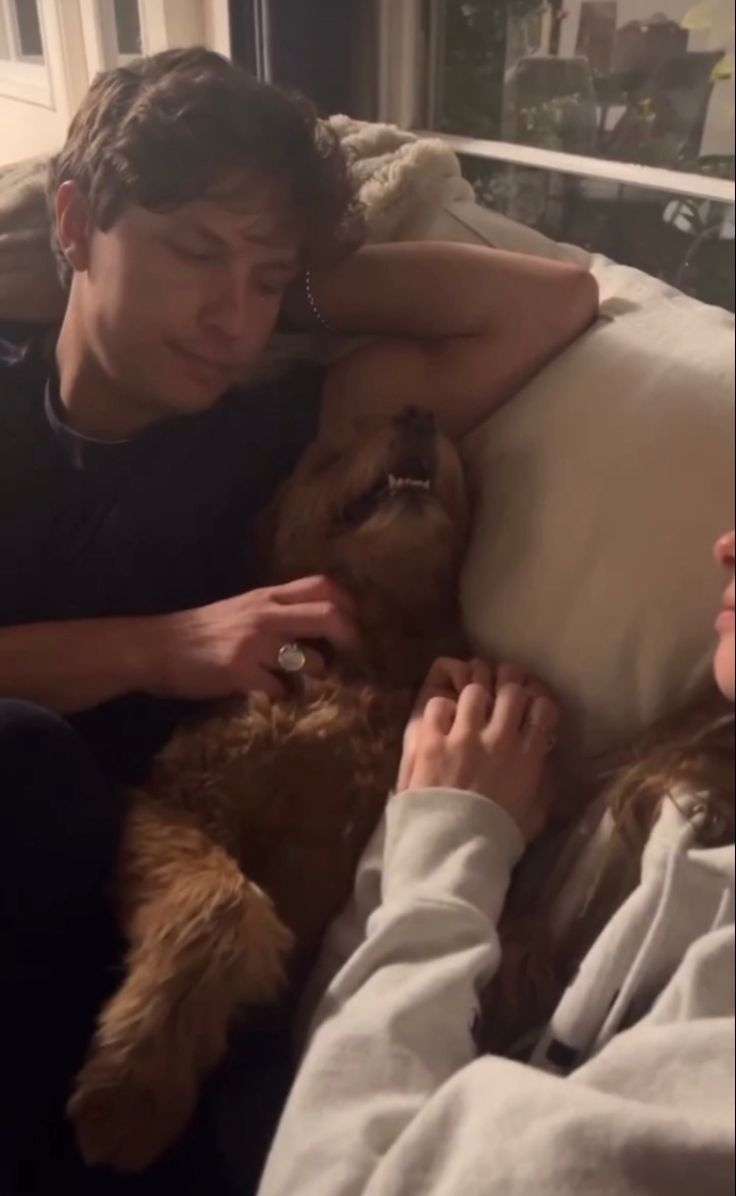 a man and woman cuddle on the couch with their dog, who is laying next to them