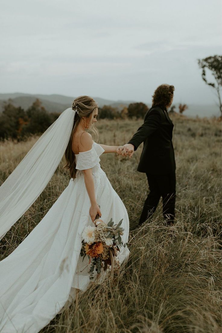 a bride and groom holding hands walking through tall grass