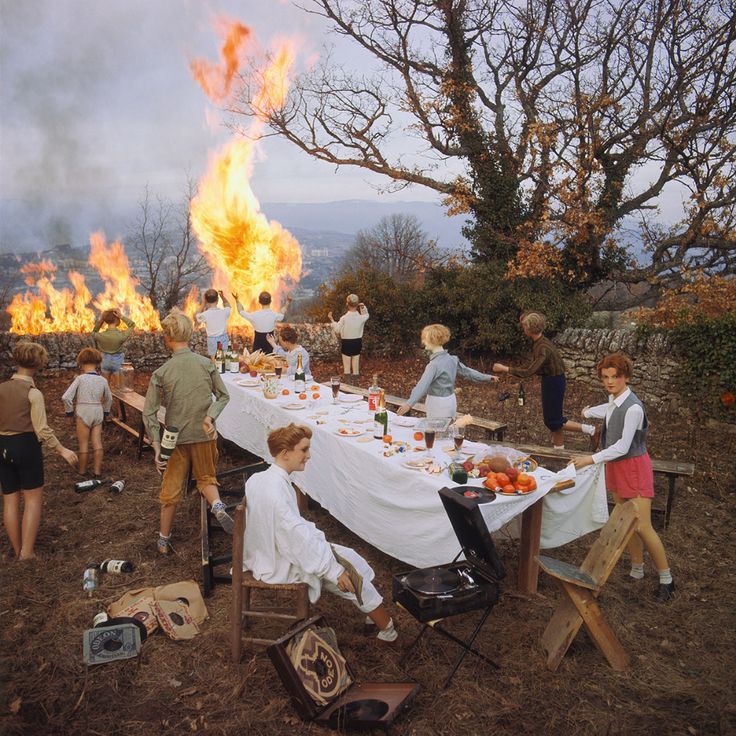 a group of people standing around a table covered in white cloths near a fire