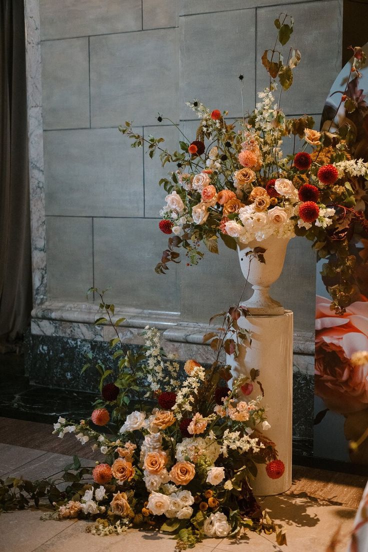 an arrangement of flowers in a vase on the ground next to a wall and window