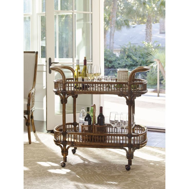 a wicker bar cart with wine bottles and glasses on it in front of a window