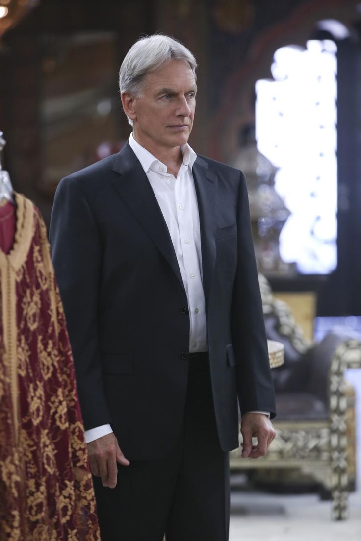 a man in a black suit and white shirt standing next to a red dress coat