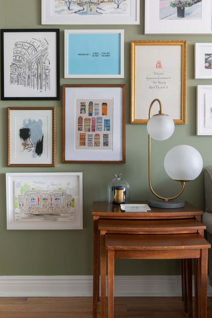 there are many framed pictures on the wall next to a small table with a lamp