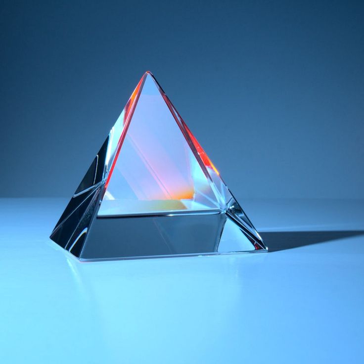 a clear glass pyramid shaped object on a blue surface with light coming from it's top