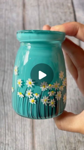 a hand holding a blue mason jar with white daisies painted on the inside and bottom