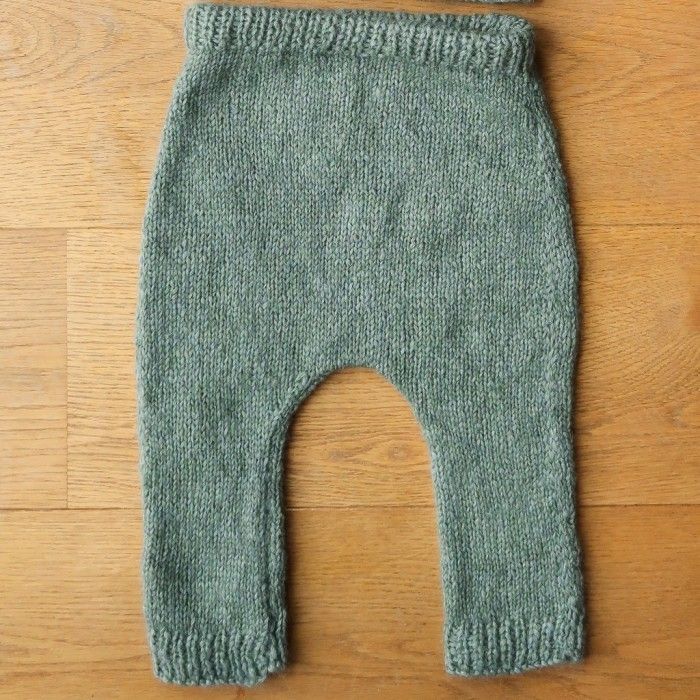 a baby's green knitted leggings laying on top of a wooden floor