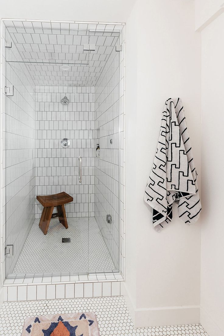 a white tiled bathroom with a bench in the shower