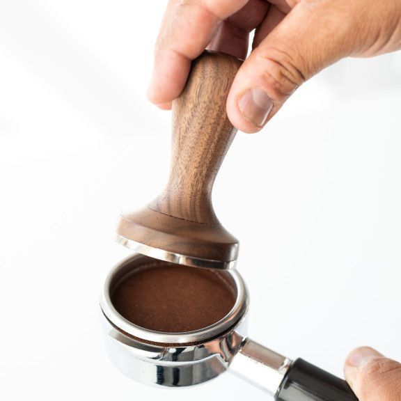 a person holding onto a metal container with brown liquid in it and a wooden handle