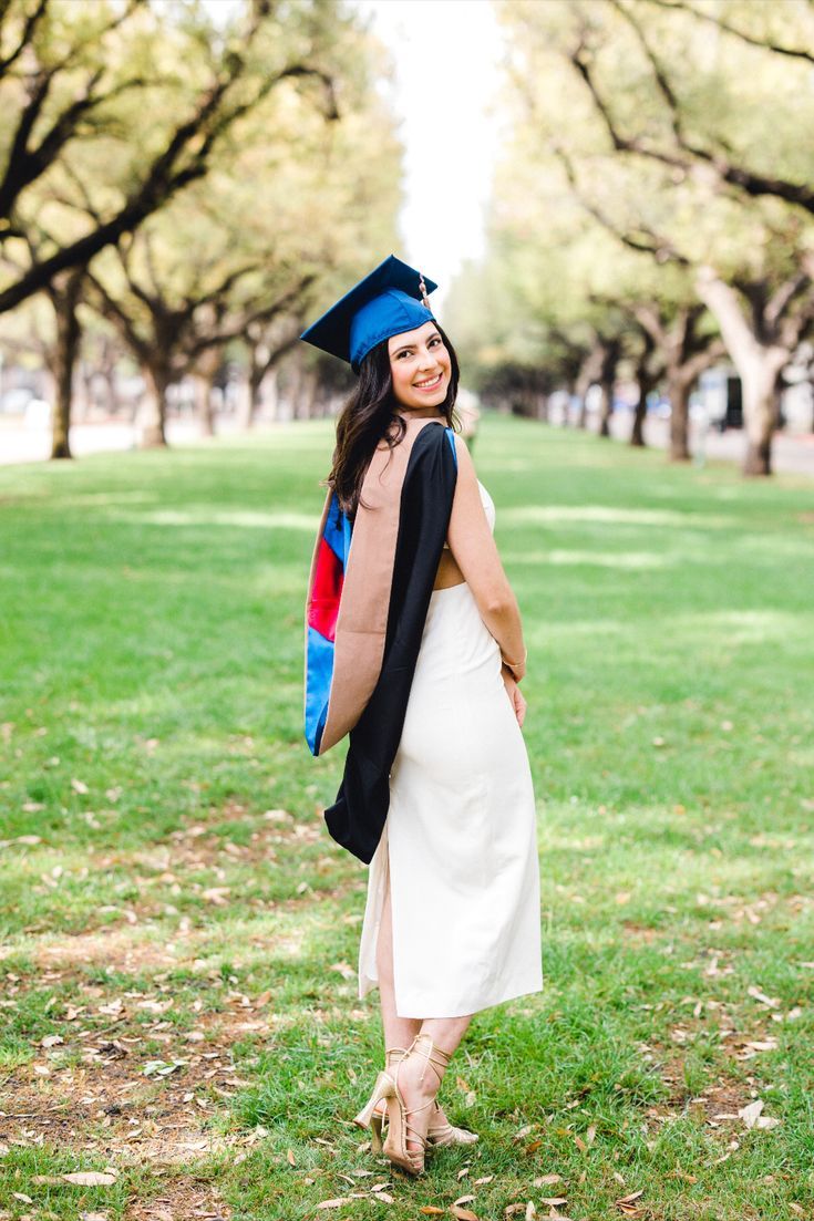 a woman wearing a graduation cap and gown is standing in the grass with her back to the camera