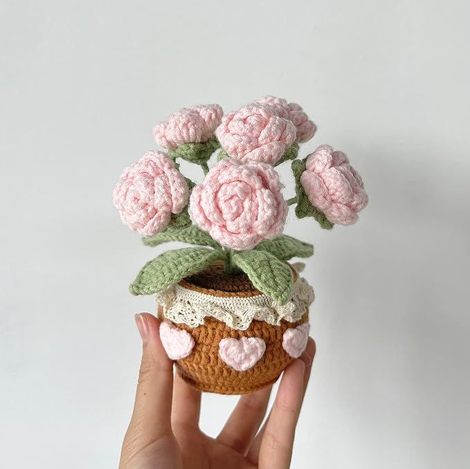 a crocheted flower pot with pink flowers in it is held up by a hand