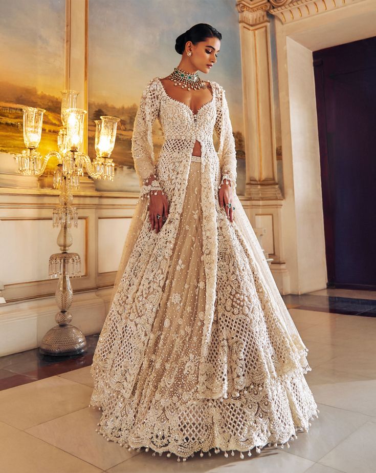 This jacket lehenga set features intricate pearl embroidery interspersed with delicate cut work on a nude base. The full sleeve jacket shows pearl tassels at sleeve hem and is paired with matching embroidered lehenga. The scalloped dupatta shows pearl drops.From Seema Gujral's Falaknuma collection. DELIVERY TIMEPlease allow 8-12 weeks for your outfit to arrive. FABRIC DETAILSNet Professional cleaning only. Jacket And Lehenga, Anarkali Sets With Pearl Embroidery In Cream, Elegant Cream Choli With Sheer Dupatta, Formal Festive Lehenga With Pearl Embroidery, Elegant Off White Designer Choli, Elegant Off-white Designer Choli, Elegant Beige Choli With Sheer Dupatta, Elegant Designer Wear Off White Lehenga, Elegant Cream Choli For Designer Wear