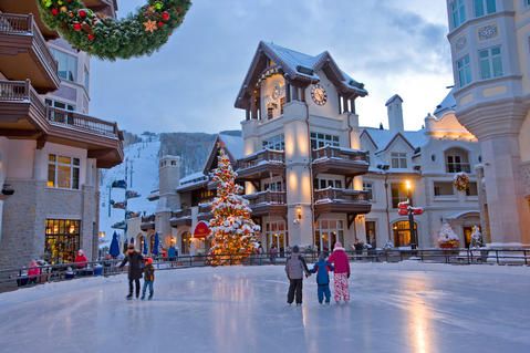 people are skating on an ice rink in front of buildings with christmas decorations and wreaths