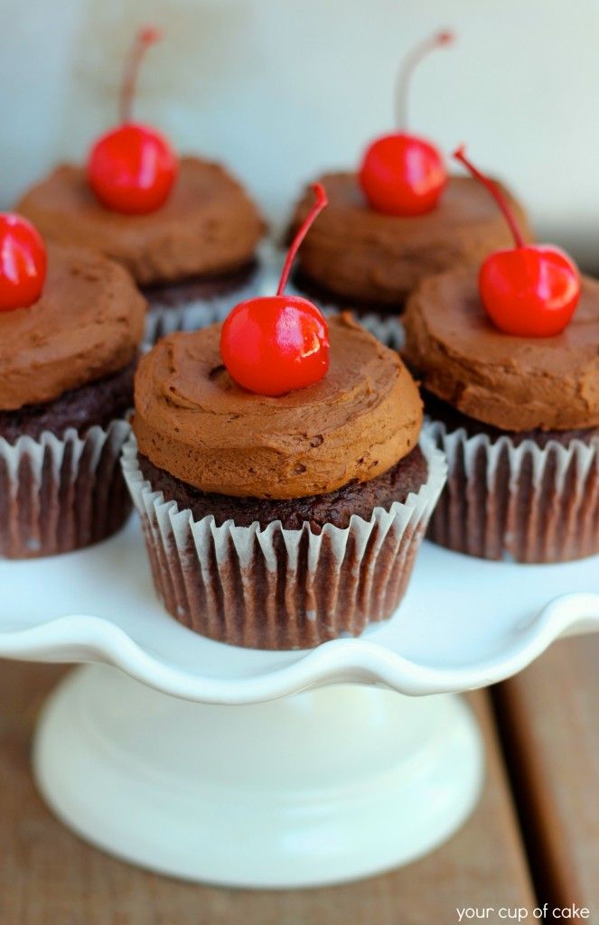 cupcakes with chocolate frosting and cherries are on a white platter