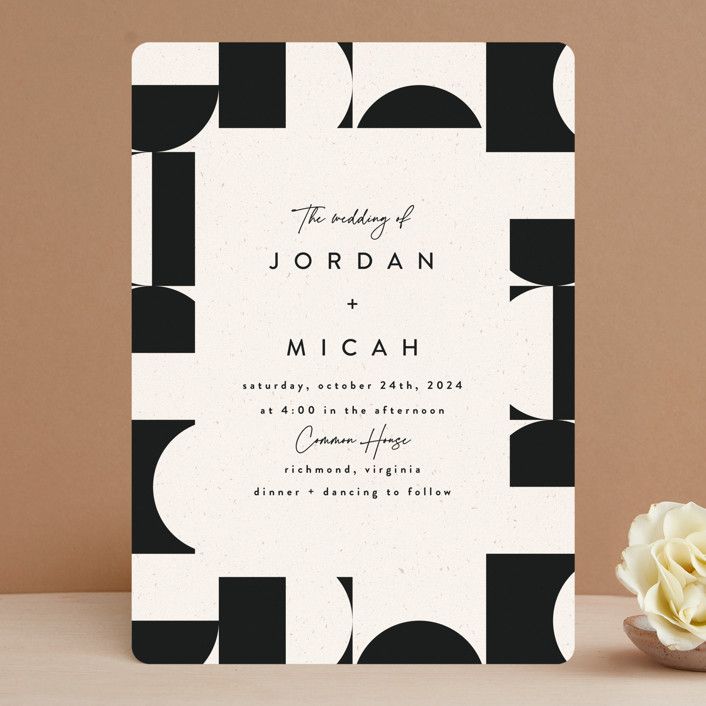 a black and white wedding card on a table next to a vase