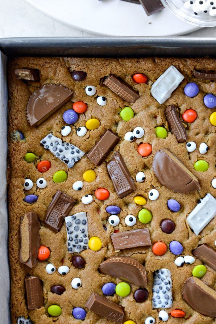 a cookie with chocolate, candy and eyeballs on it in a baking pan next to a spoon