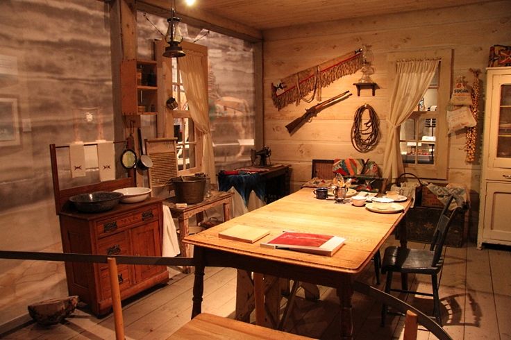 a table and chairs in a room with wooden walls on the wall behind it is an old fashioned kitchen