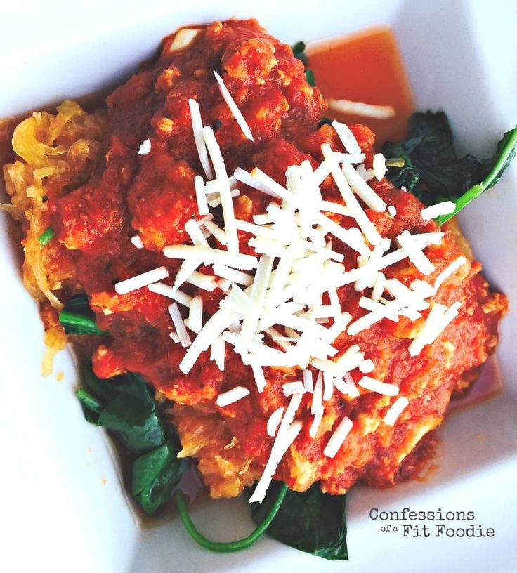 a white bowl filled with pasta and spinach covered in sauce, cheese and parmesan