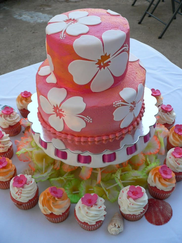 a three tiered cake with flowers on it sitting on top of a table next to cupcakes