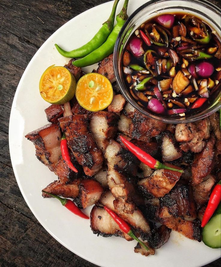 a white plate topped with meat and veggies next to a bowl of sauce