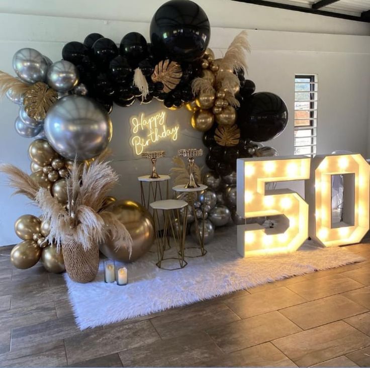 a 50th birthday party with balloons and lights on the wall, gold and black decorations