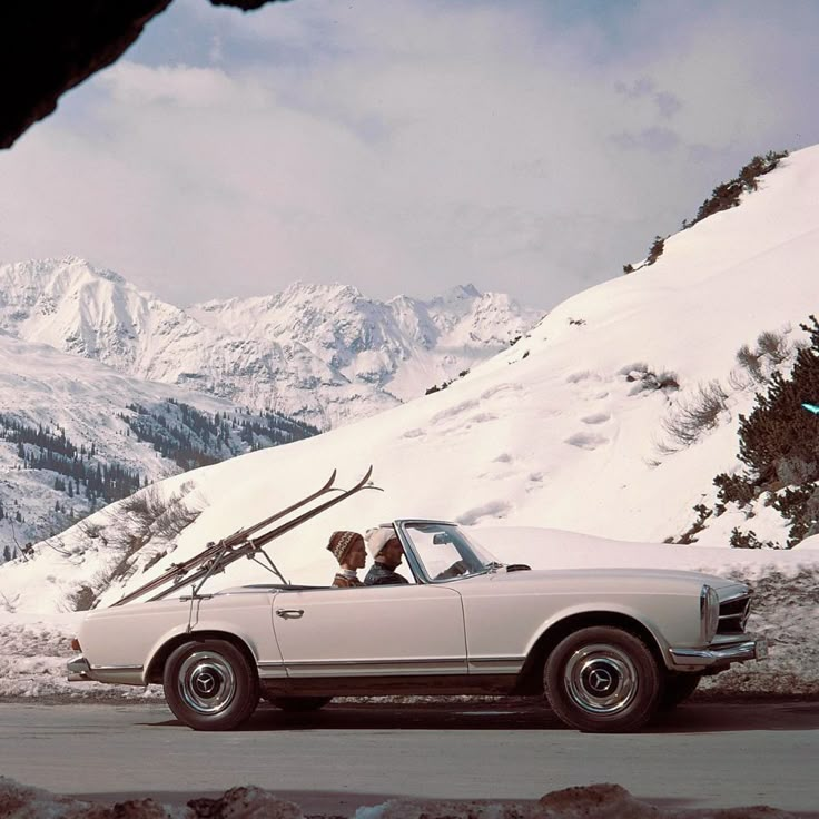 a white car parked on the side of a snow covered road with mountains in the background