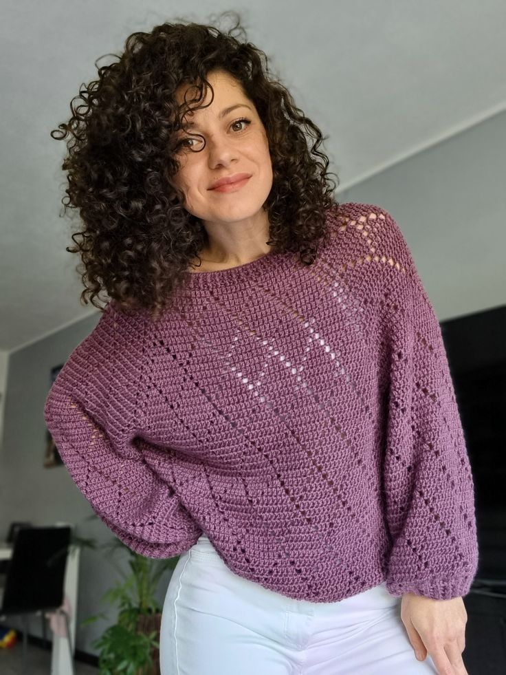 a woman with curly hair wearing a purple sweater and white pants, posing for the camera