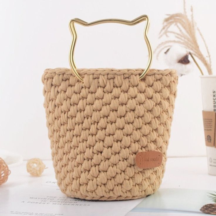 a straw bag with a gold handle on top of a table next to a cup