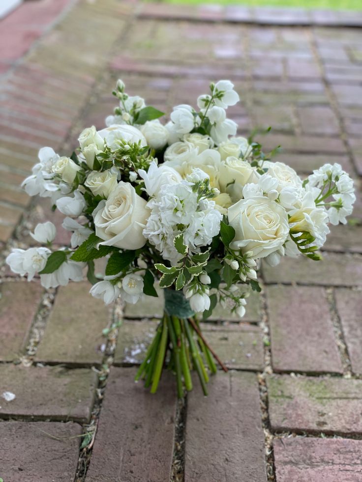 a bouquet of white flowers sitting on top of a brick floor next to a sidewalk