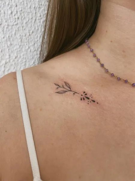 the back of a woman's shoulder with a small flower tattoo on her chest