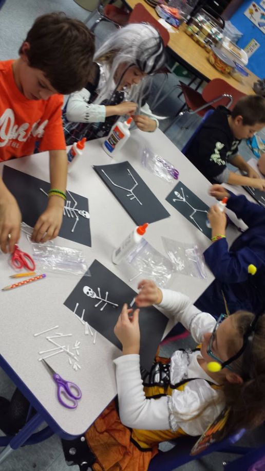 several children are sitting at a table with scissors and writing on black paper in front of them