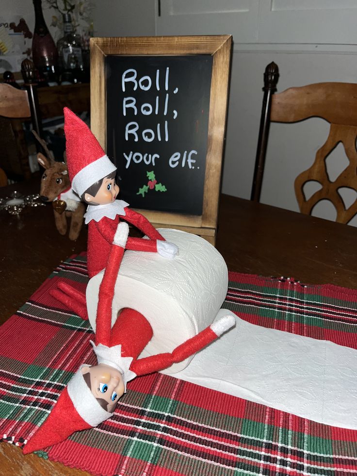 an elf sitting on top of a roll of toilet paper next to a chalkboard