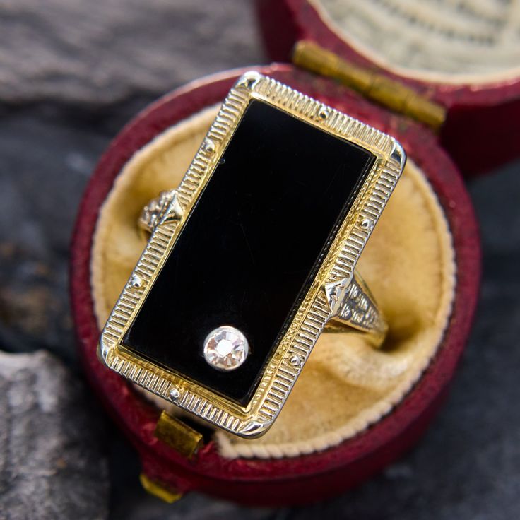 a ring with a black stone on it in a red velvet case, sitting on top of a rock