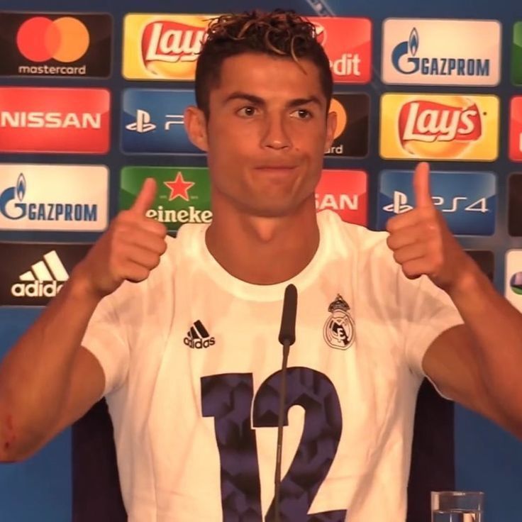 a young man giving the thumbs up in front of a wall with soccer balls on it