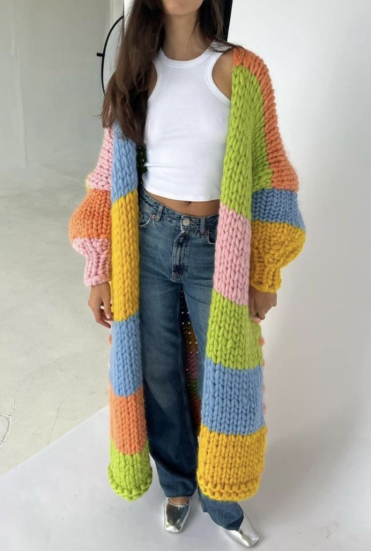 a woman standing in front of a white wall wearing a colorful knitted cardigan