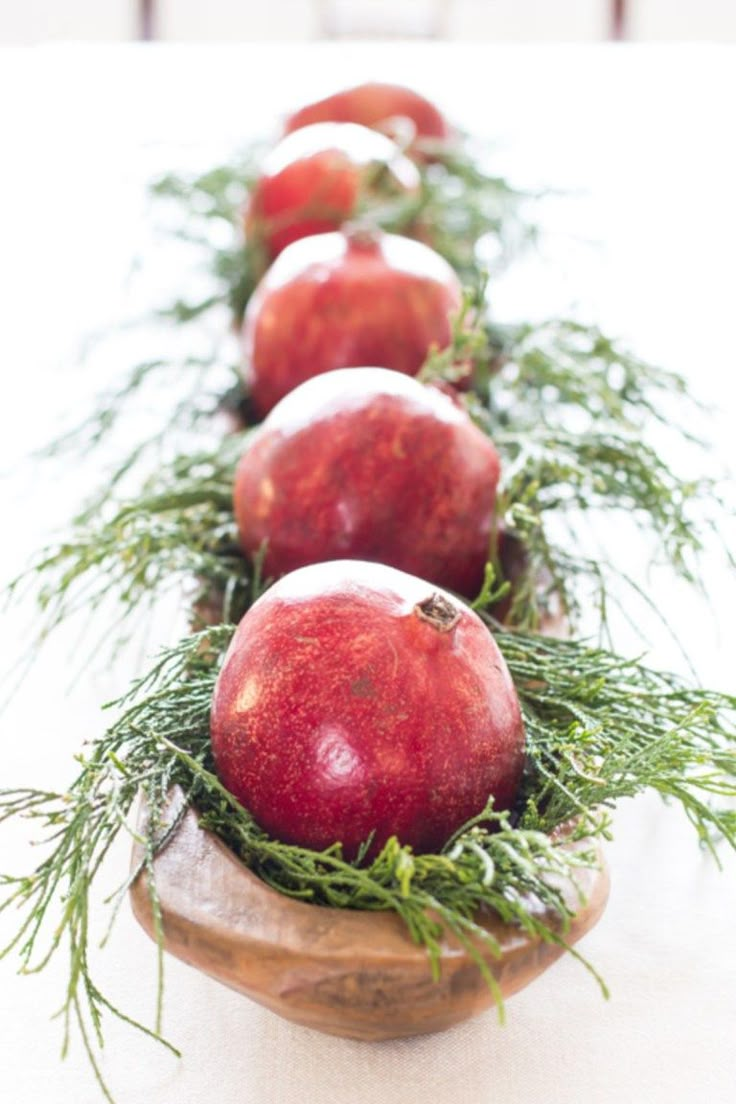 apples and other fruit are arranged in a row on a wooden platter with greenery