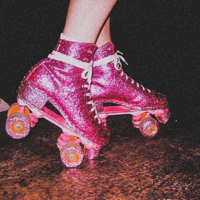 pink roller skates with white laces on them and one person's feet in the background