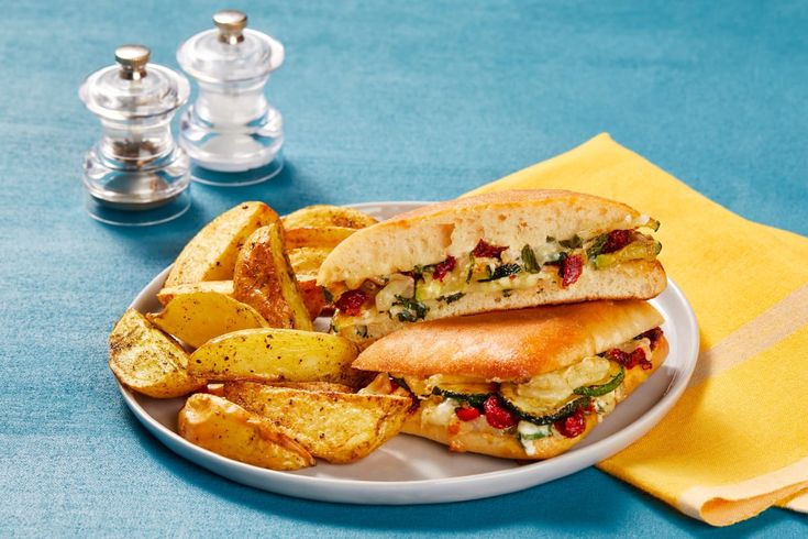 a sandwich and some potato wedges on a white plate with a blue tablecloth