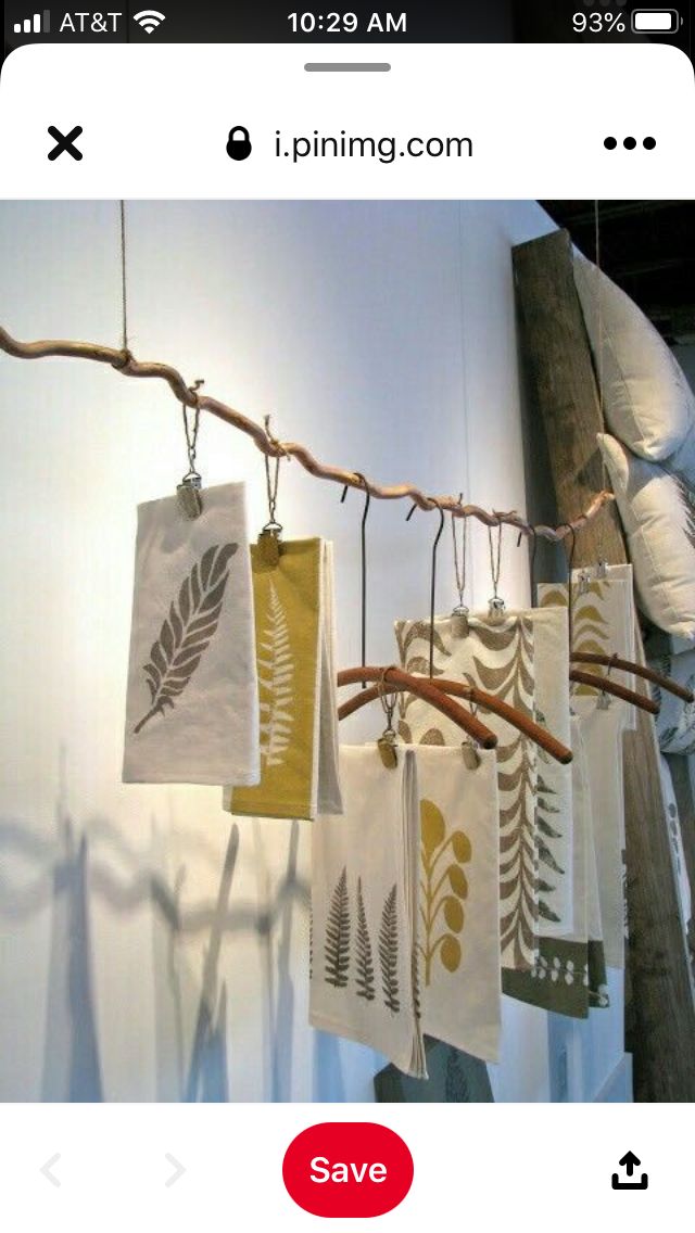 several tea towels hanging from a branch in front of a white wall with leaves on them