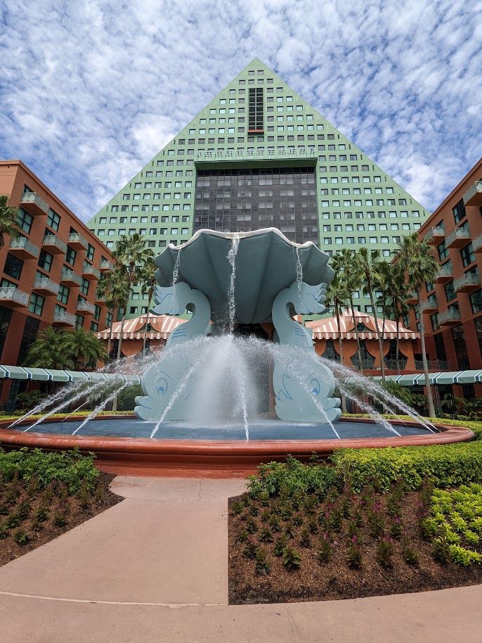 an elephant fountain in front of a large building with palm trees and bushes around it