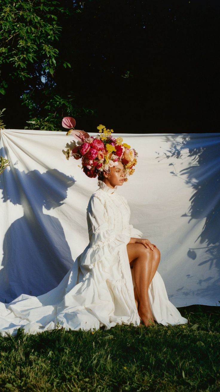 a woman sitting on top of a grass covered field next to a white cloth wall