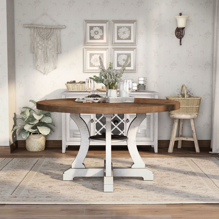 a dining room table with two chairs and pictures on the wall behind it, in front of a potted plant