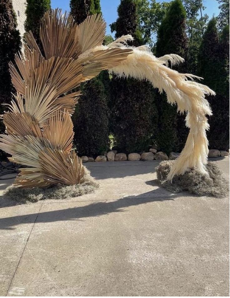 an outdoor sculpture made out of dried grass and palm leaves in front of a house